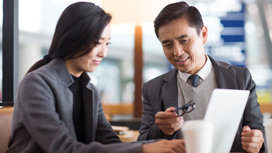 two men look at laptop; the image used for Overseas Investment Plan